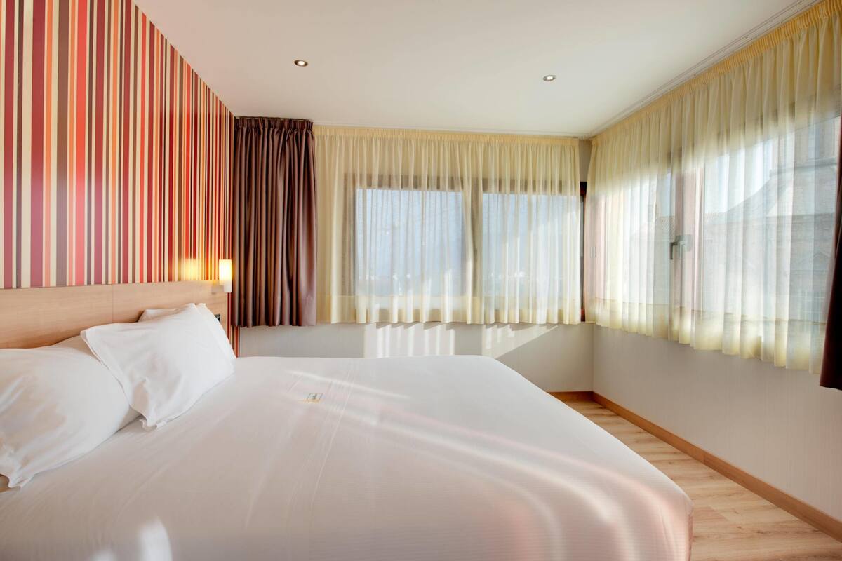 A large bed with white linens, a wooden headboard, and a wall with vertical stripes.