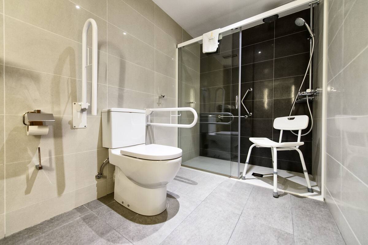 A modern bathroom with a toilet, a shower area with a glass door, and a white chair.