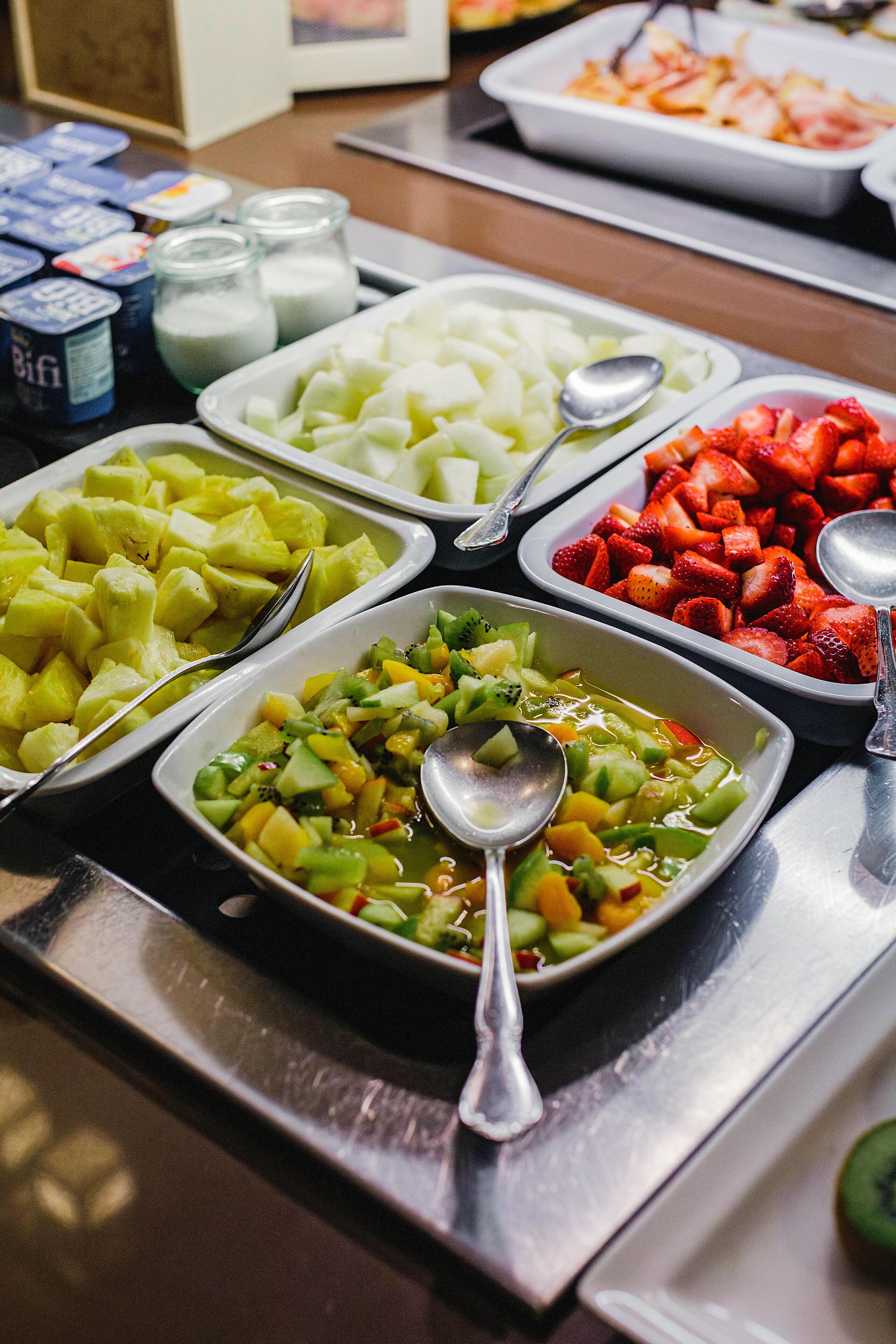 A buffet with various fruit and vegetable dishes, including pineapple, kiwi, and strawberries.