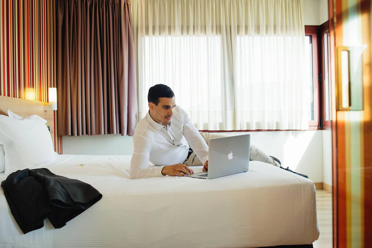 A hotel room with a bed, a laptop, and a coat on the bed.
