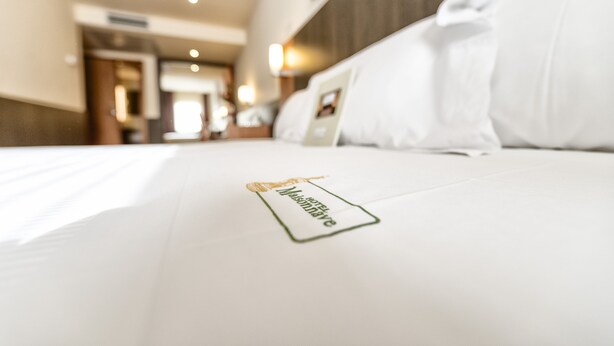 Una camera d'albergo con un letto rifatto, un cuscino con etichetta e una testiera in legno.