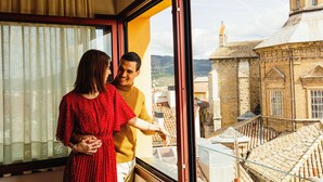 Una coppia in piedi vicino a una finestra con vista su una città e edifici storici.