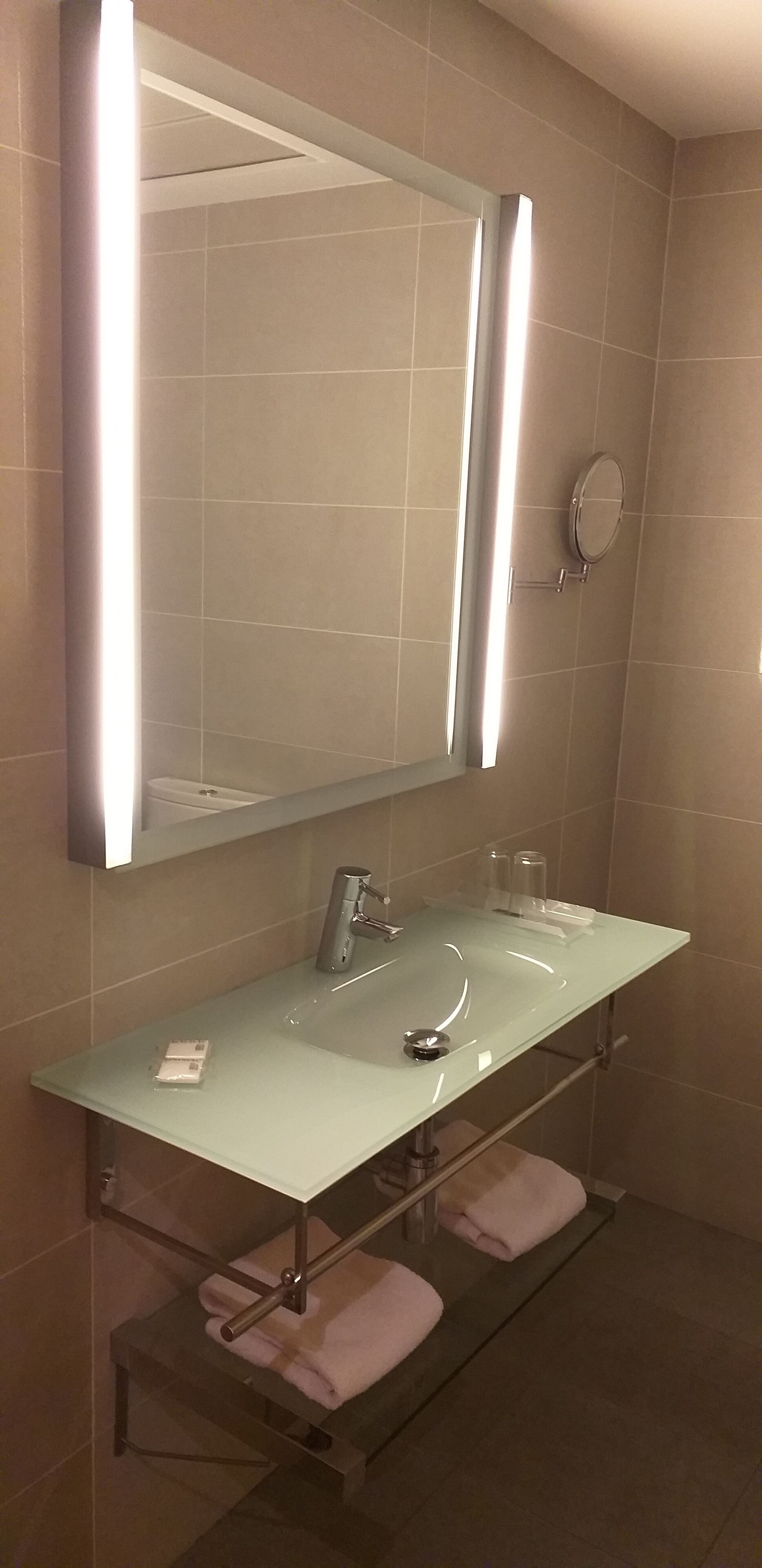 Un baño moderno con un lavabo de vidrio, un espejo grande y un perchero para toallas.