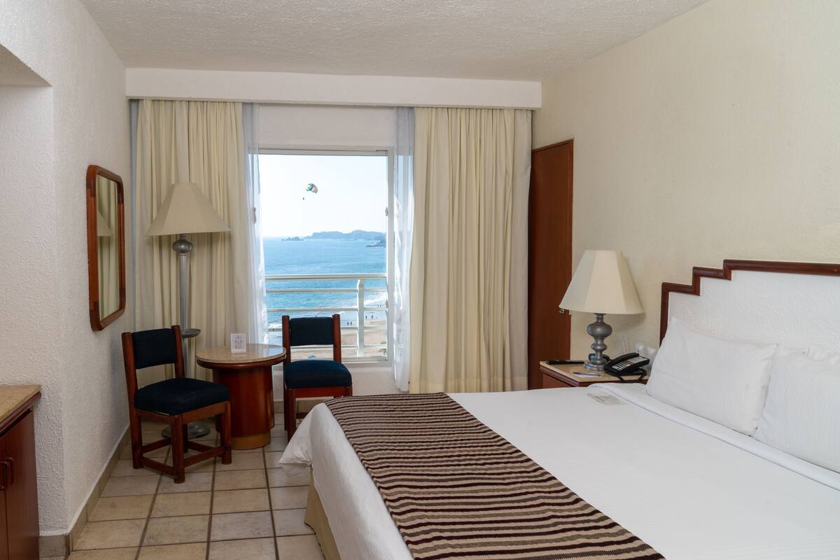 Habitación de hotel con cama, escritorio, silla, una mesita y vista al mar.