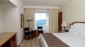 Habitación de hotel con cama, escritorio, silla, una mesita y vista al mar.