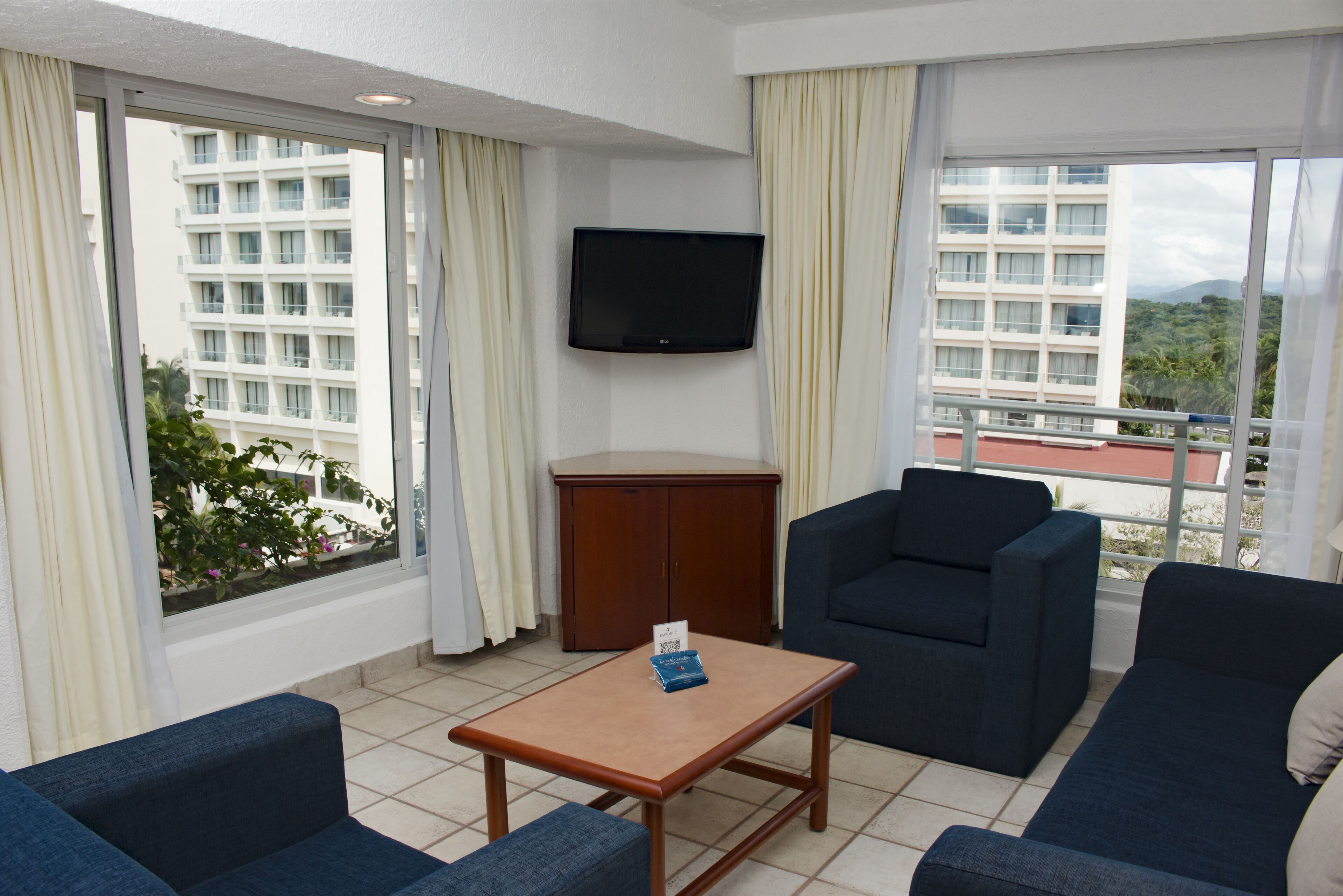 Ein Hotelzimmer mit großem Fenster, einem Flachbildfernseher, einem Holztisch und zwei blauen Sofas.