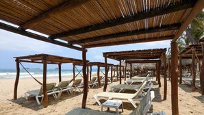 Una playa con pérgolas de madera y sillas de descanso blancas.