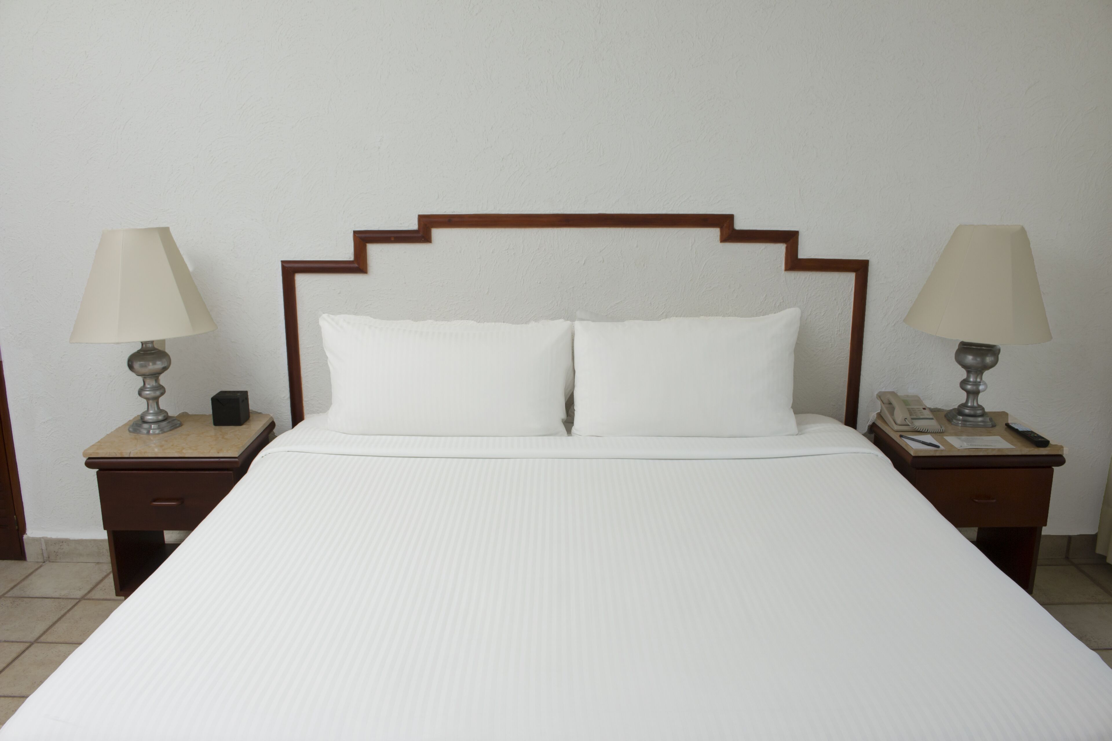 A neatly made bed with white linens, two bedside tables with lamps, and a wooden headboard.