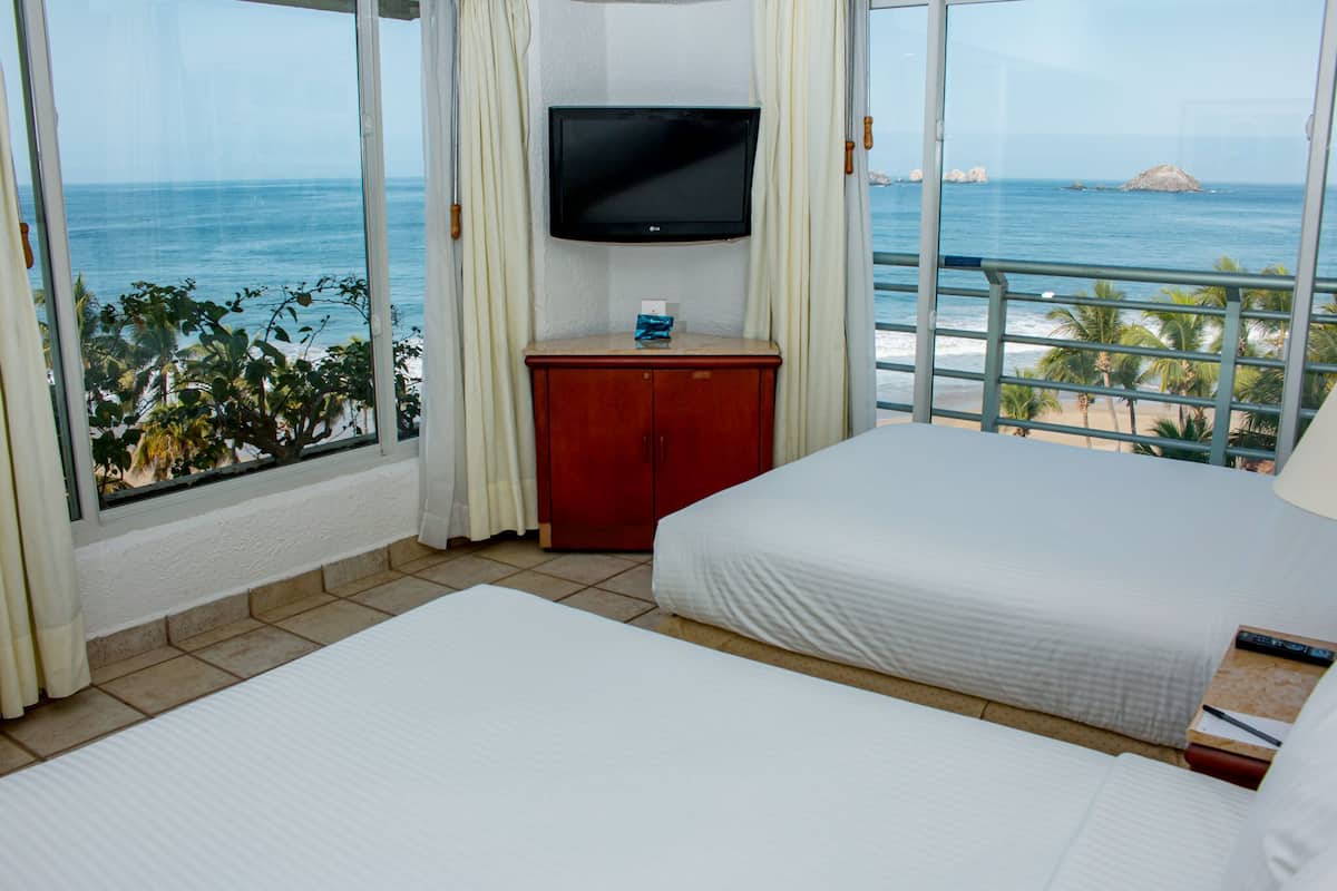 Habitación de hotel con dos camas, un televisor, un pequeño armario rojo y vista al océano.