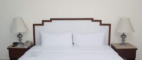 A neatly made bed with white linens, two bedside tables with lamps, and a wooden headboard.