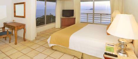 Une chambre d’hôtel avec un lit, une télévision, un bureau et une vue sur la mer.