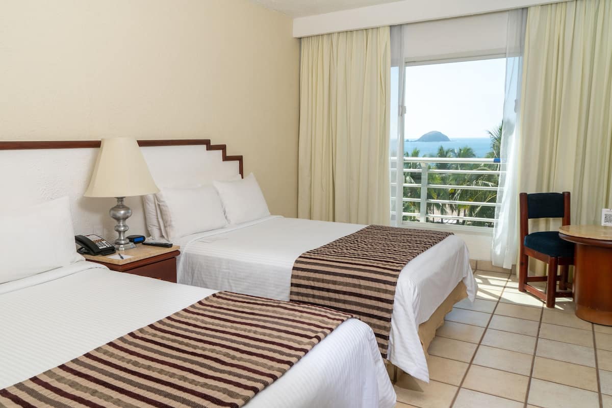 Habitación de hotel con dos camas, una mesita de noche con lámpara, teléfono y una silla.