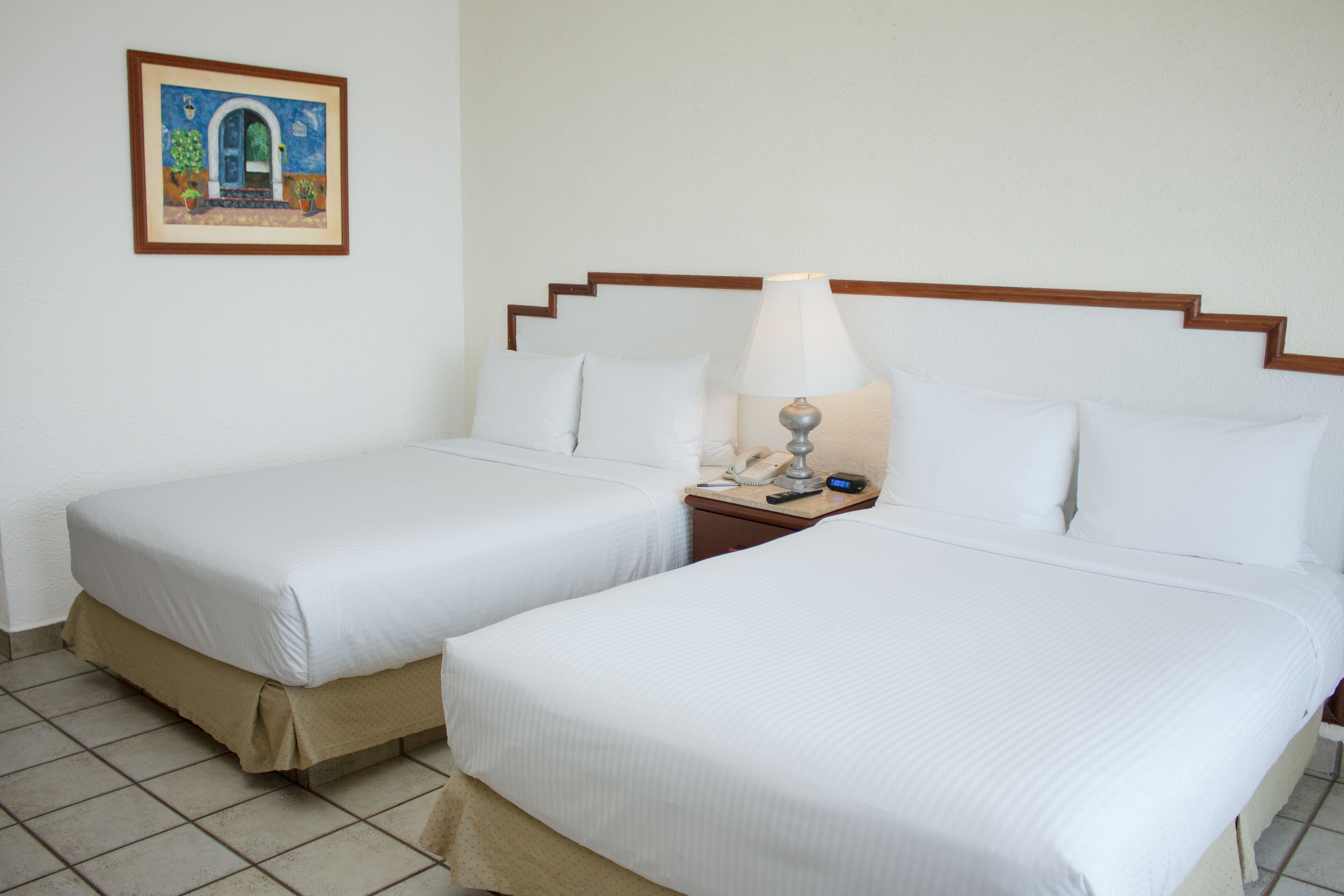 A hotel room with two beds, a nightstand with a lamp, and a framed picture on the wall.