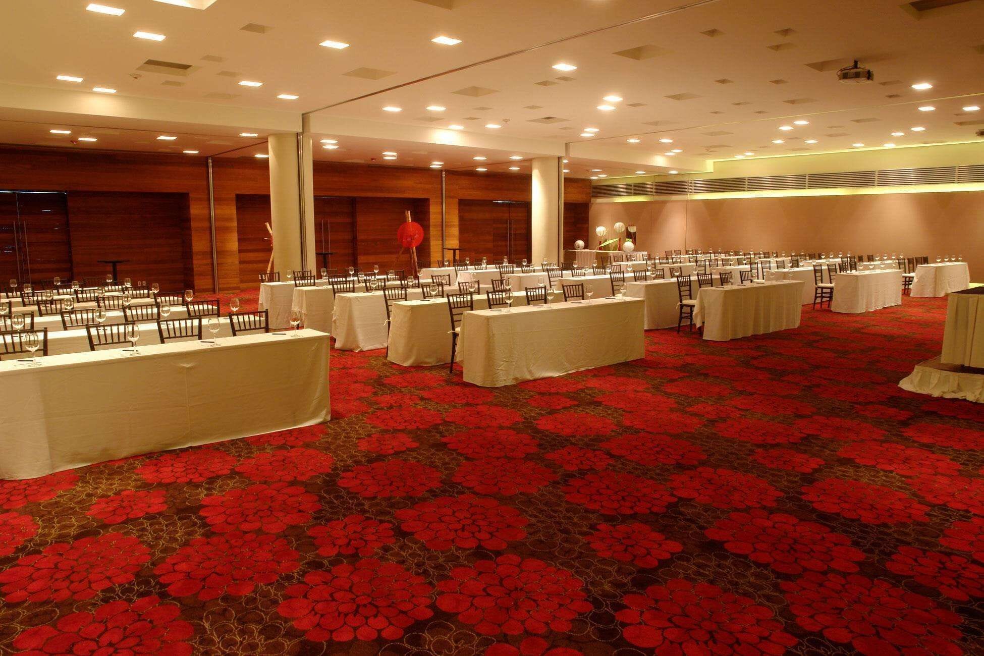 A banquet hall with multiple round tables covered with white tablecloths, arranged in rows.