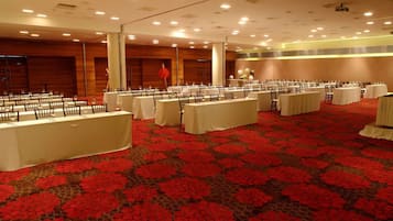 Un salón de banquetes con varias mesas redondas cubiertas con manteles blancos, dispuestas en filas.