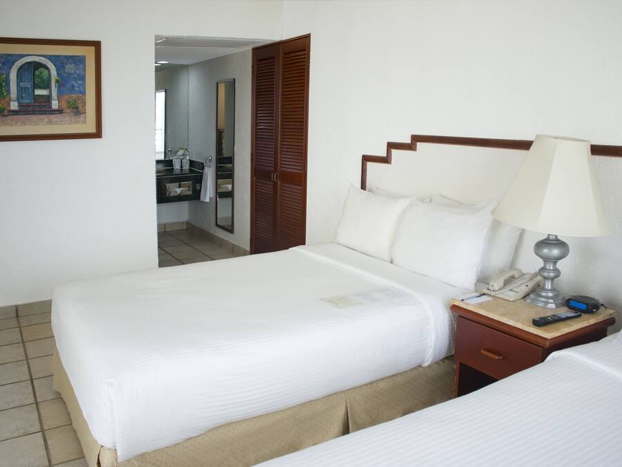 Quarto de hotel com cama, mesa de cabeceira, luminária e um quadro na parede.