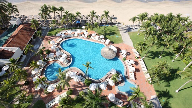 Un resort con una piscina grande, zonas de descanso y vistas a la playa.