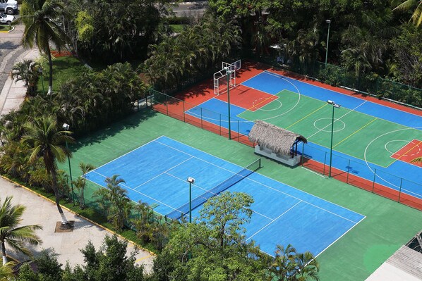 Una cancha de baloncesto al aire libre rodeada de árboles y una estructura con techo de paja.
