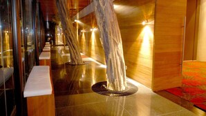 Un pasillo con paredes de madera y suelo pulido, con una serie de estructuras que recuerdan a árboles y bases reflectantes.