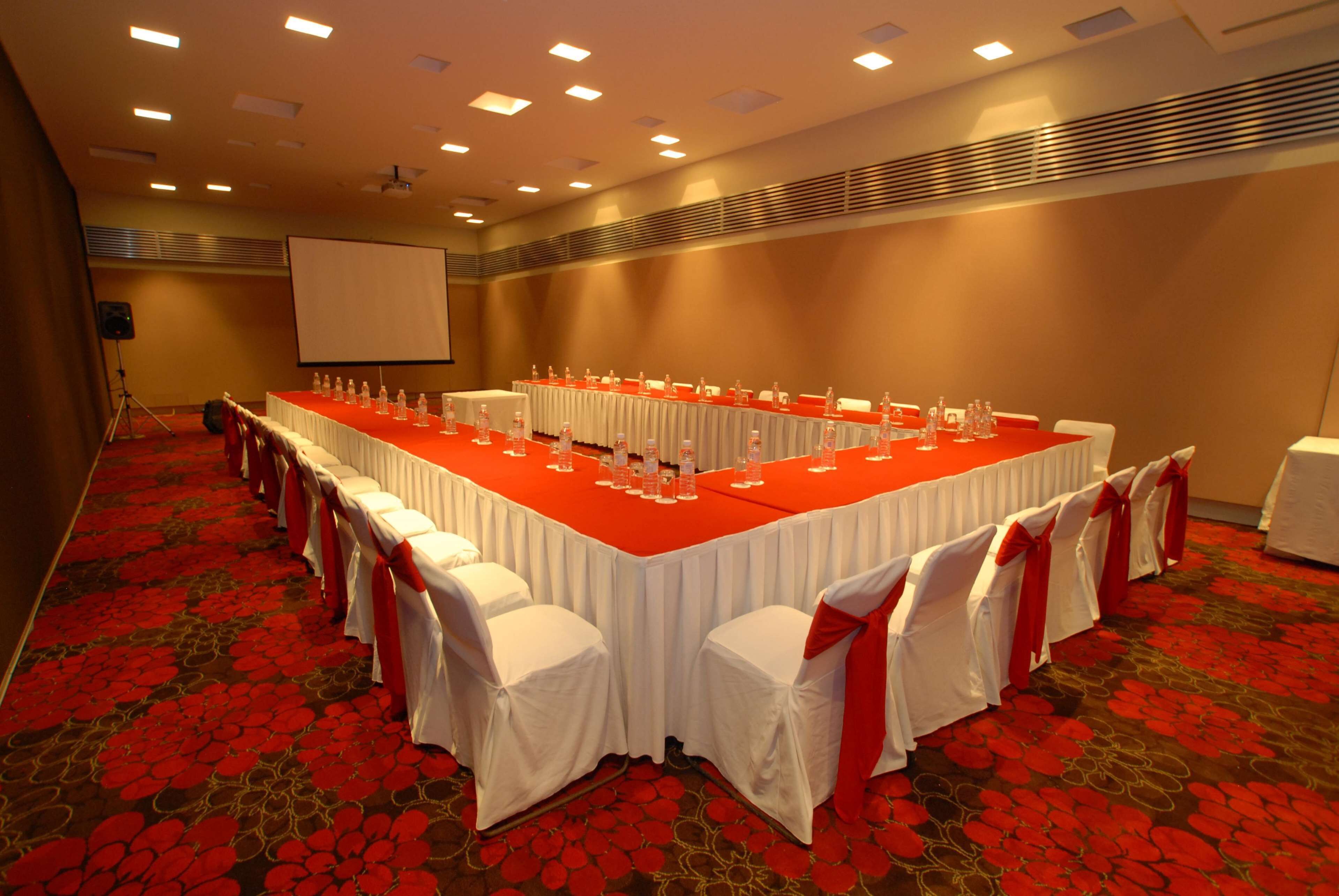 Una sala de conferencias con una mesa larga, sillas blancas y una pantalla para proyector.
