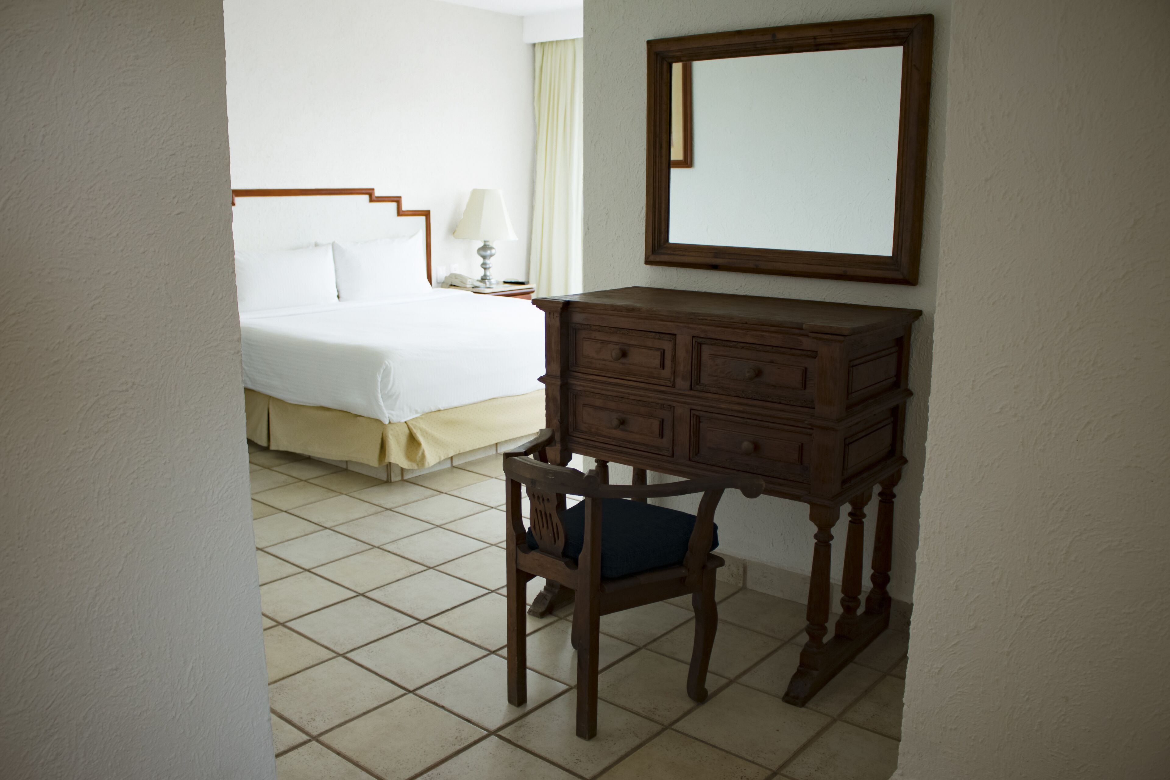 A hotel room with a bed, a wooden dresser, a chair, and a mirror on the wall.