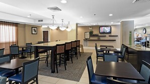 Une salle à manger d’hôtel avec plusieurs tables et chaises, un comptoir de réception et un écran de télévision.