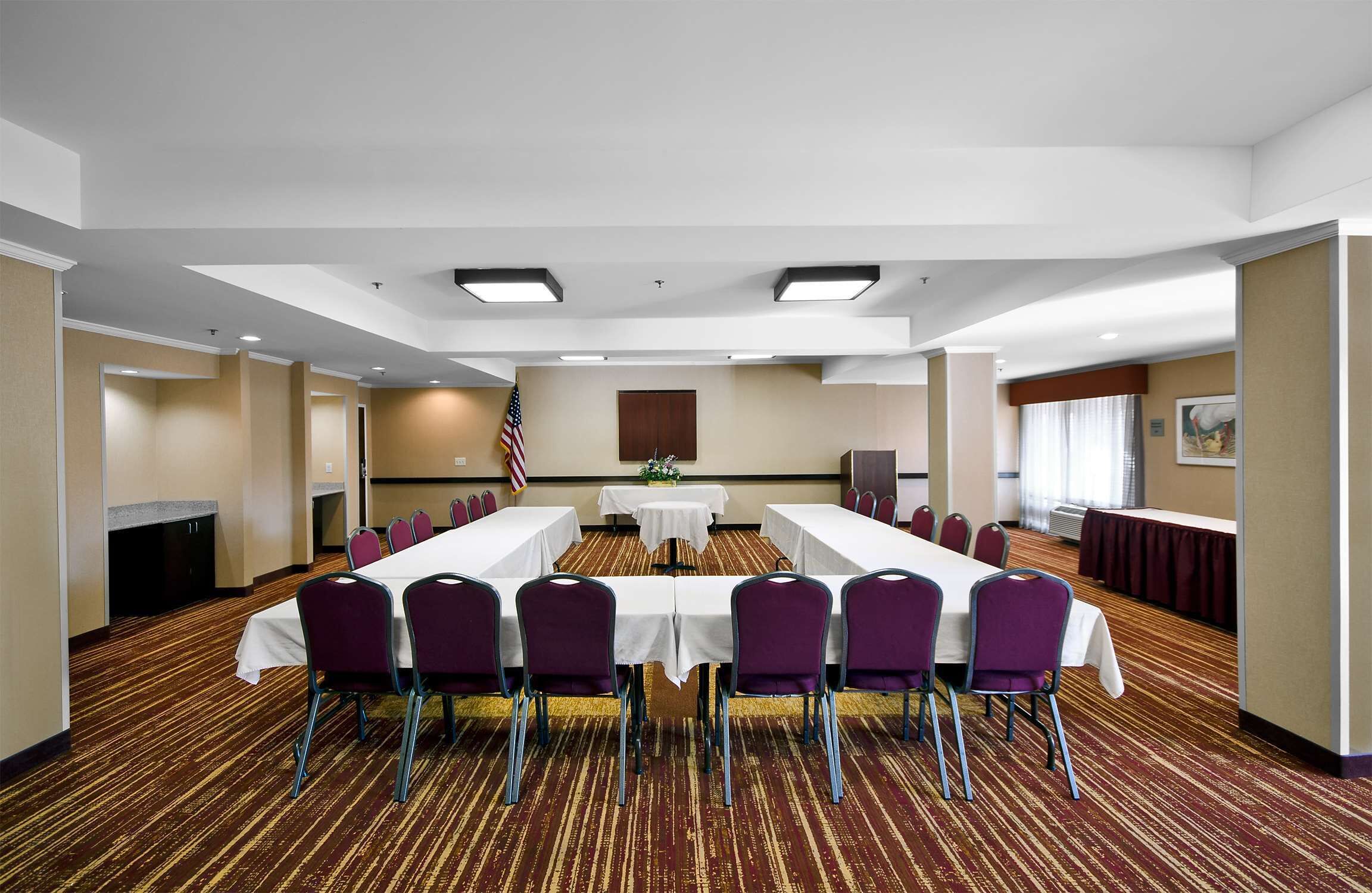 A conference room with a long table, purple chairs, and a carpeted floor.