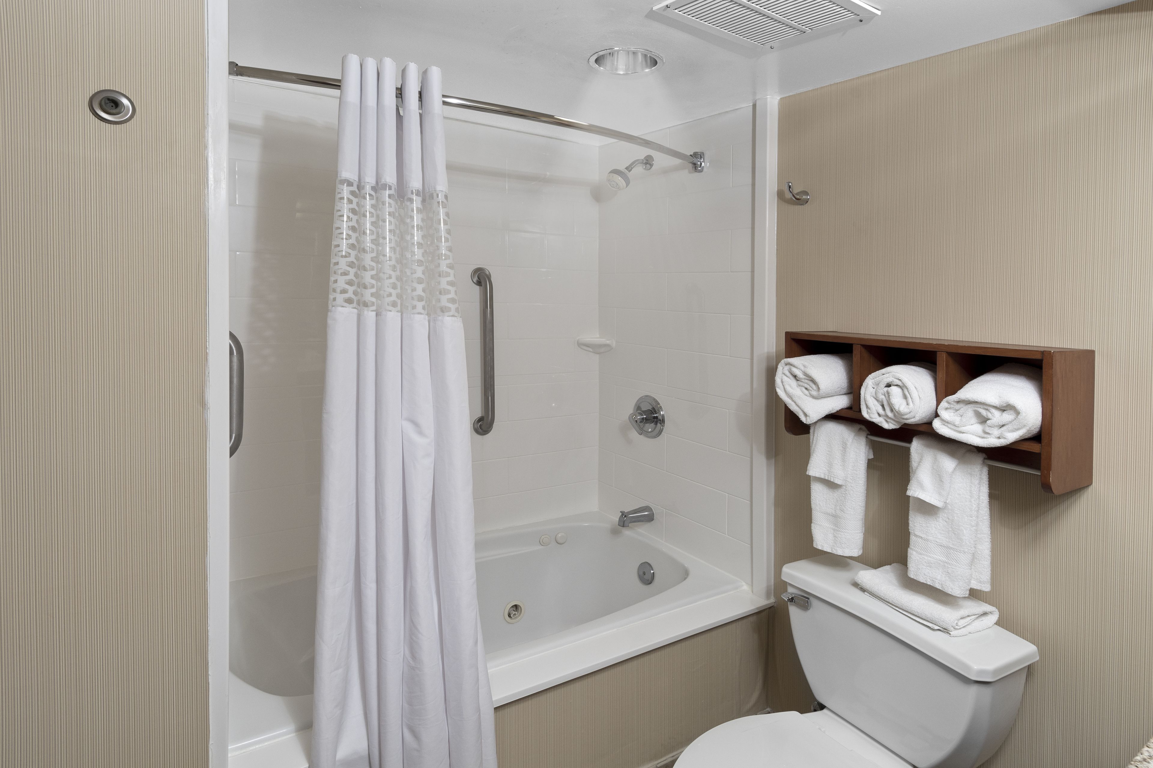 A bathroom with a shower, bathtub, toilet, and a towel rack with neatly folded towels.