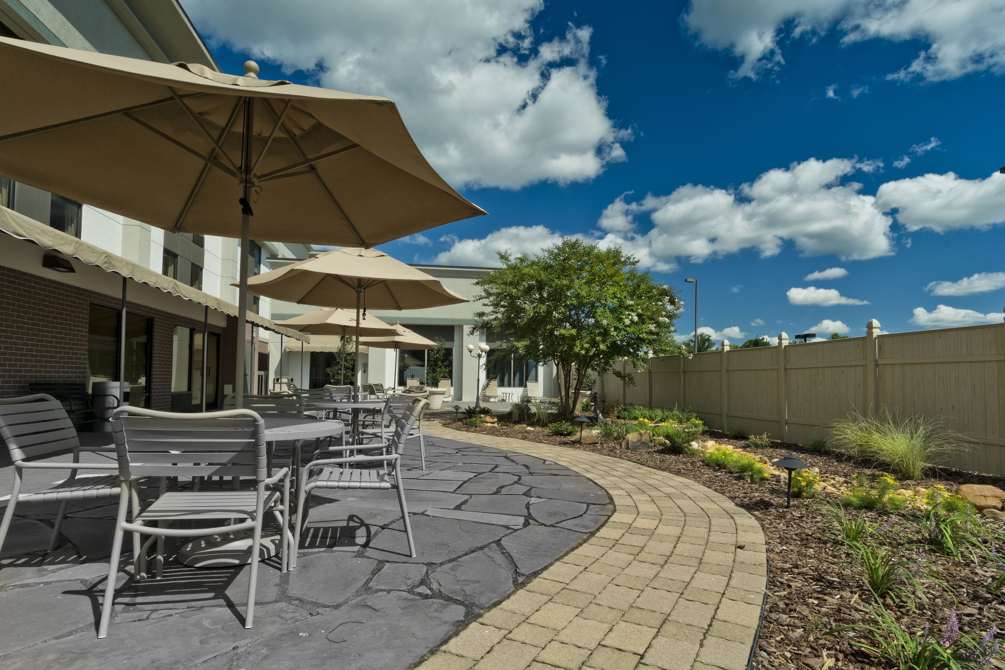 An outdoor patio with tables and chairs, surrounded by a brick pathway and a wooden fence.