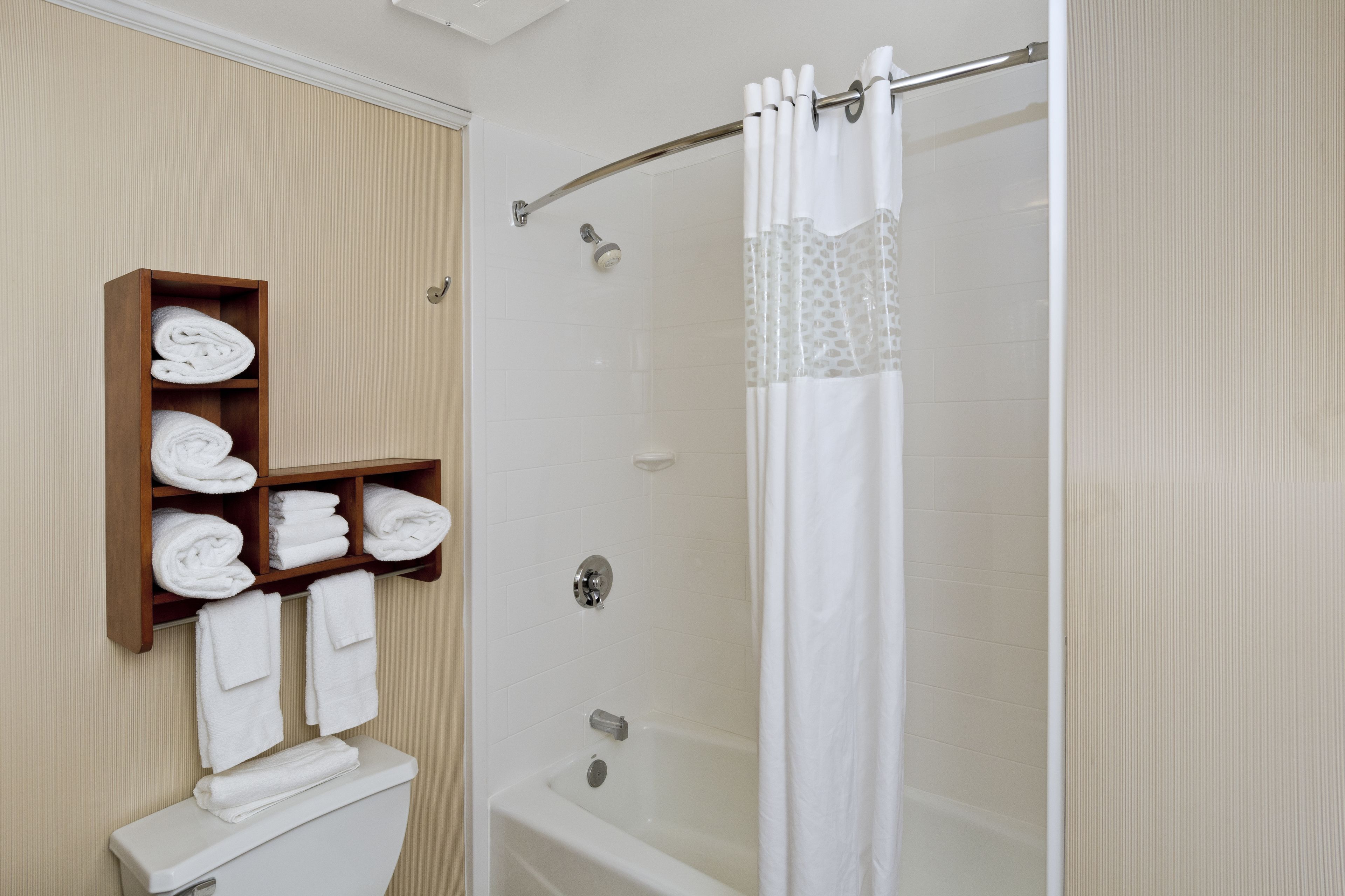A bathroom with a shower, a toilet, and a wooden shelf with towels.