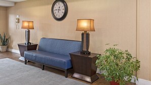A lobby with a blue sofa, two lamps, a clock, and a potted plant.