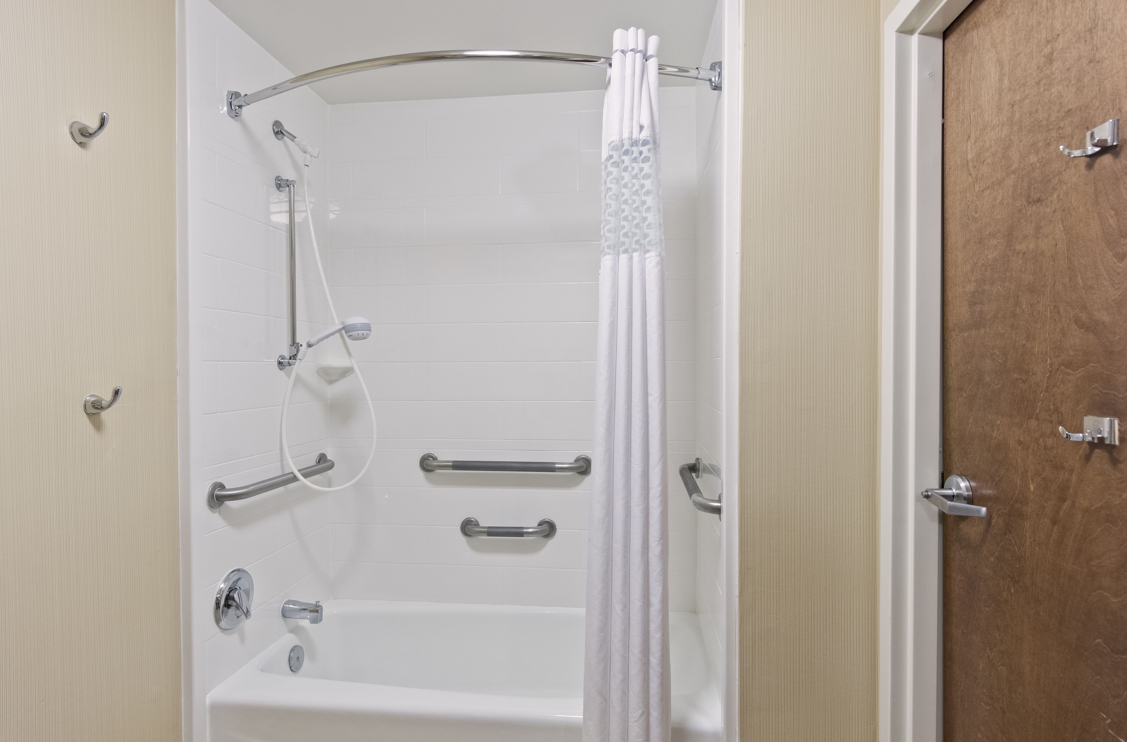 A bathroom with a bathtub, shower, and toilet. It includes grab bars and a shower curtain.