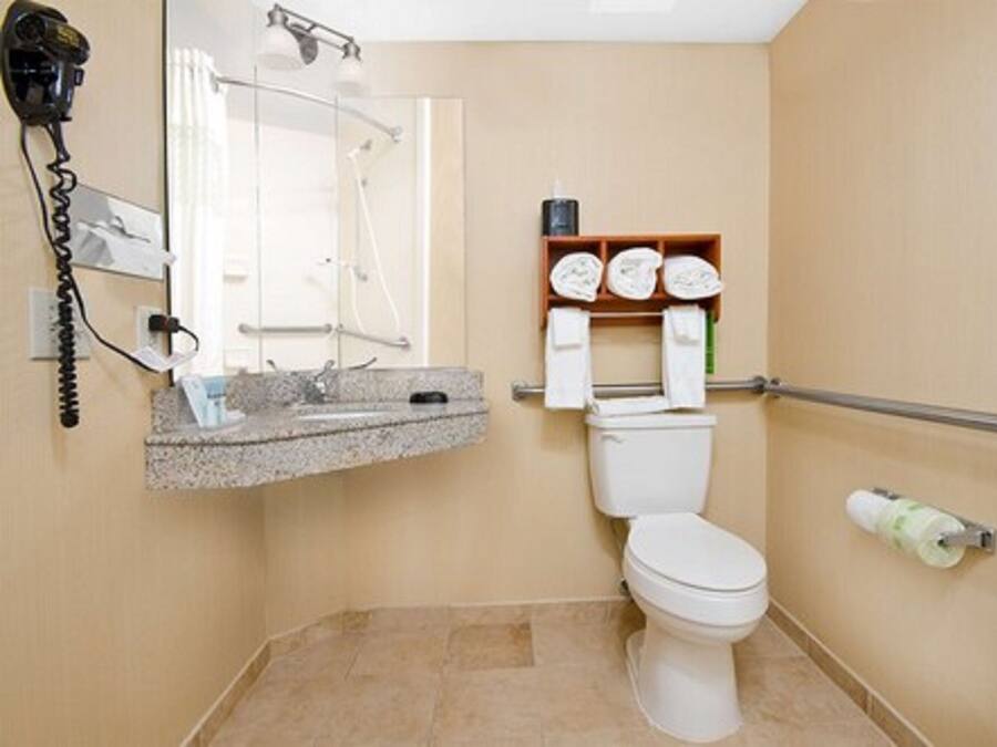 A bathroom with a toilet, a sink with a towel rack, and a hairdryer on the wall.