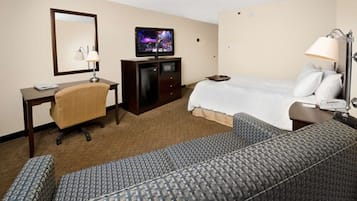Una habitación de hotel con cama, escritorio, silla, televisor y lámpara.