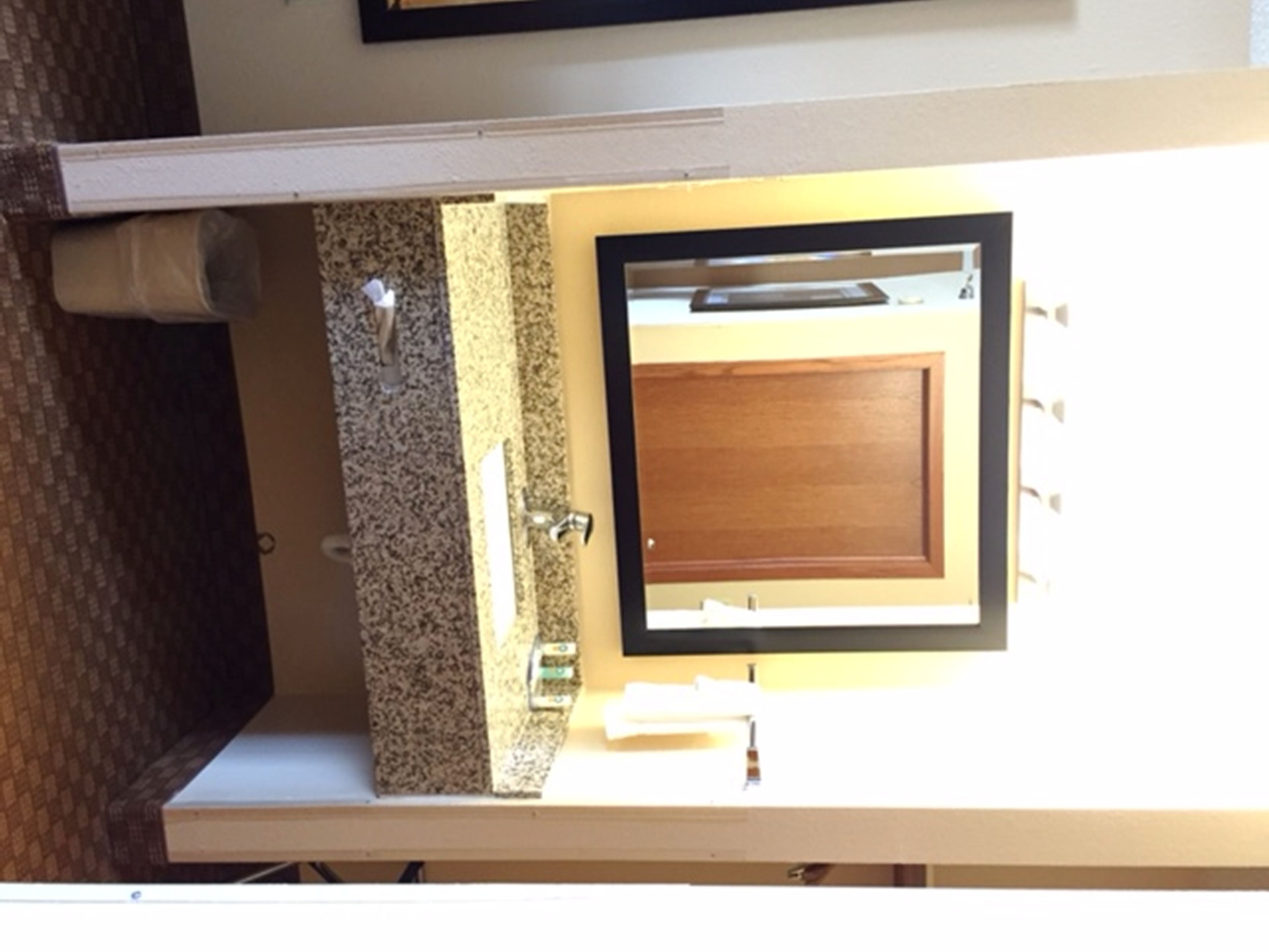 A bathroom with a granite countertop, a wooden door, and a mirror.