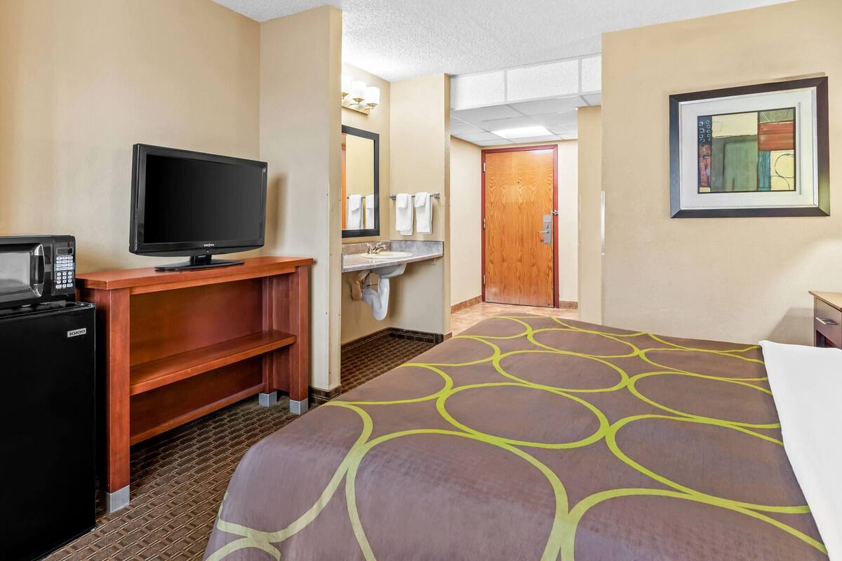 Une chambre d’hôtel équipée d’un lit, d’une télévision, d’un minibar, d’un lavabo et d’une porte donnant sur une autre pièce.