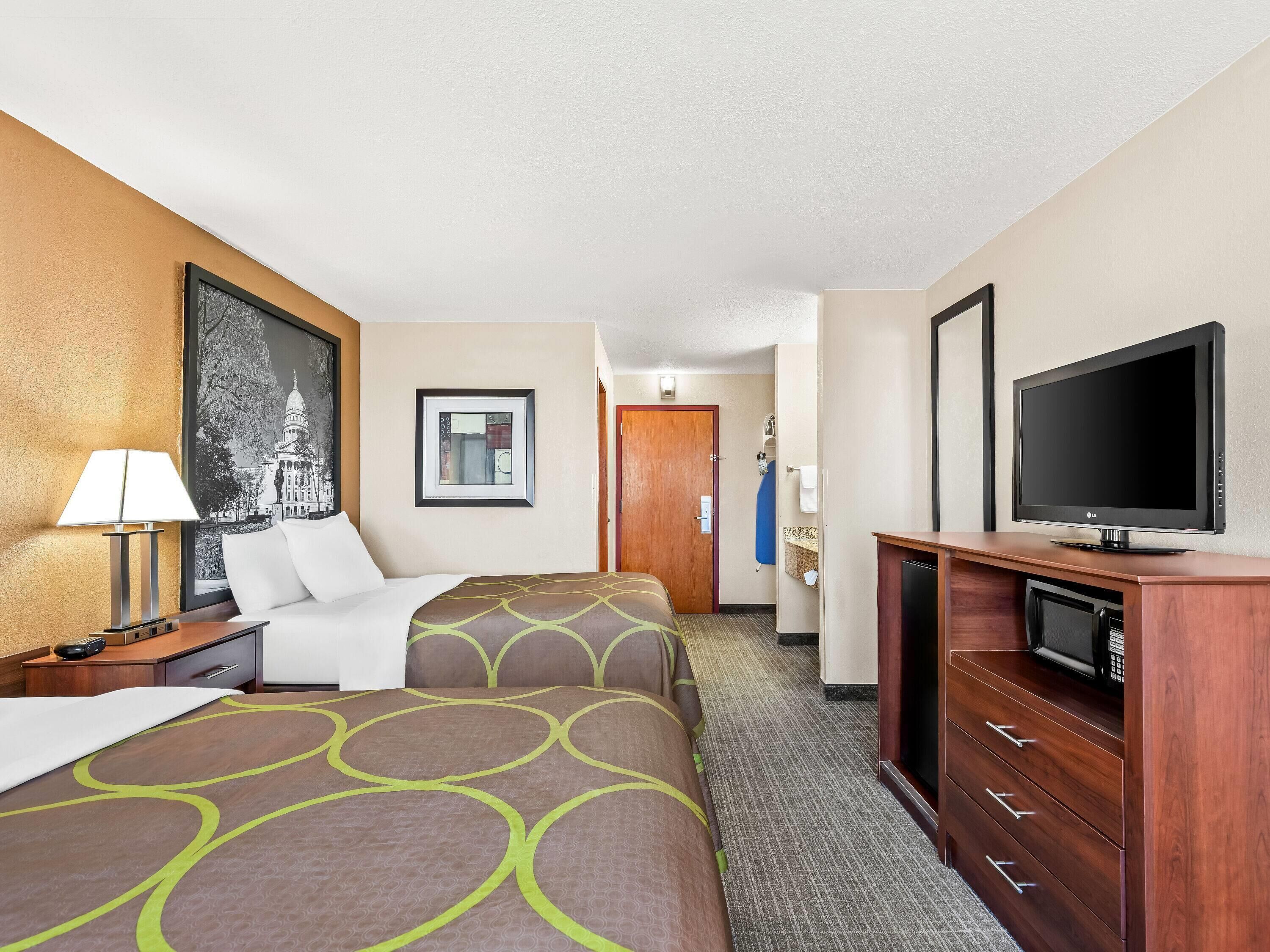 A hotel room with two beds, a TV, a desk with a lamp, and a framed picture on the wall.