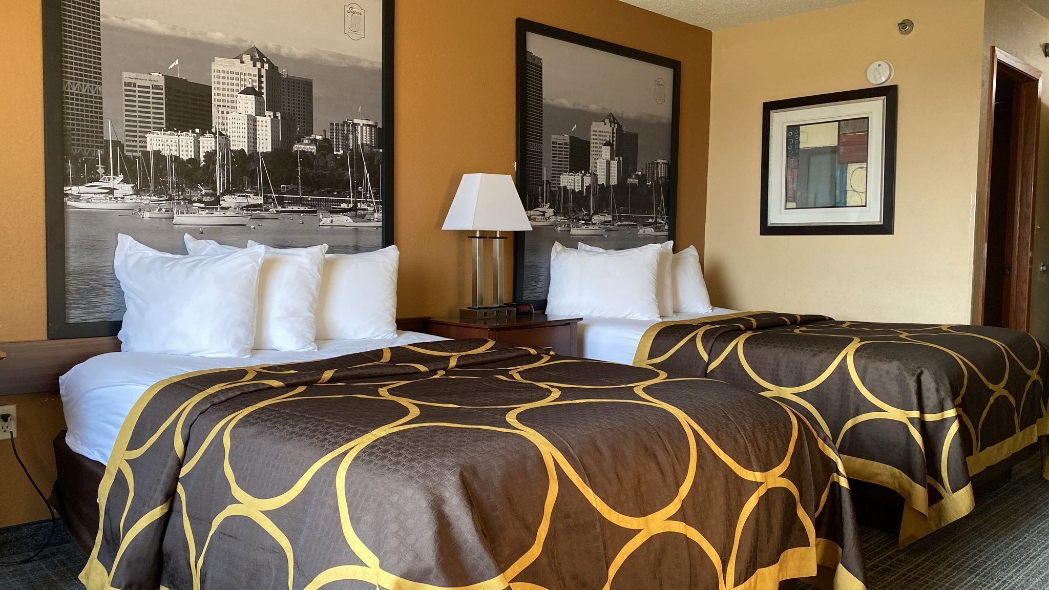 A hotel room with two beds, a cityscape view, a lamp, and a framed picture on the wall.