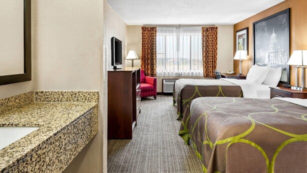 A hotel room with a large bed, a smaller bed, a desk with a TV, a desk lamp, a chair, and a large window with curtains. - Super 8 by Wyndham Sturtevant/Racine (Sturtevant)