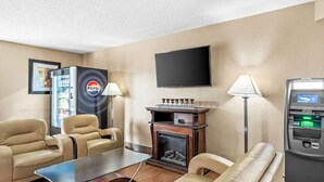 A hotel room with beige walls, a flat-screen TV, a fireplace, a Pepsi refrigerator, a cash machine, and two leather sofas. - Super 8 by Wyndham Sturtevant/Racine (Sturtevant)