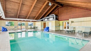 A swimming pool with a wooden ceiling and tiled walls, surrounded by seating and a covered area. - Super 8 by Wyndham Sturtevant/Racine (Sturtevant)