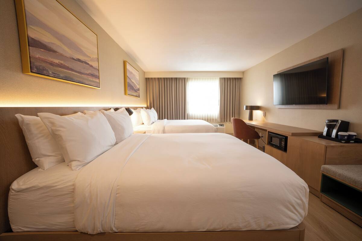 A hotel room with two beds, a desk, a TV, and a window with curtains.