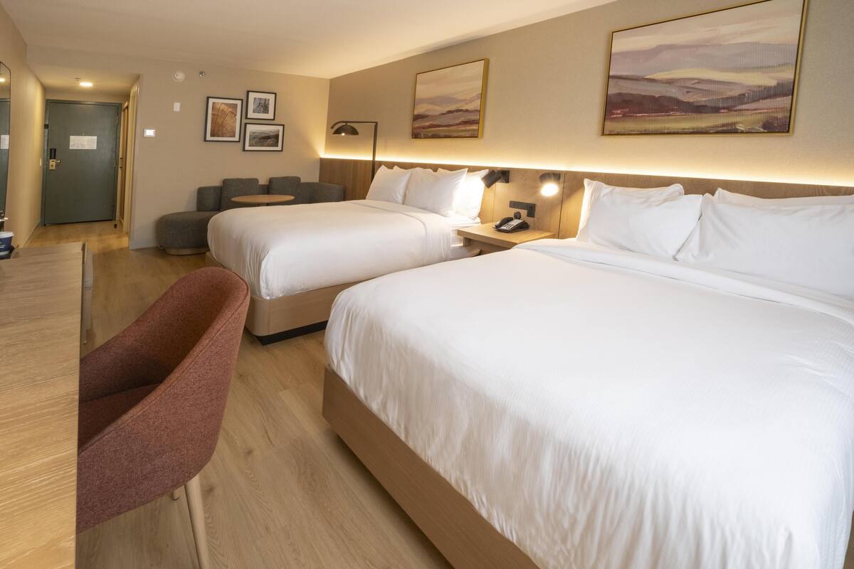 A hotel room with two beds, a desk, a chair, and artwork on the walls.