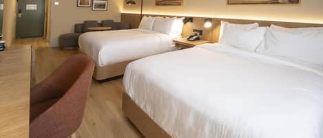A hotel room with two beds, a desk, a chair, and artwork on the walls.