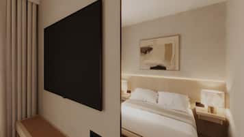 A hotel room with a flat-screen TV mounted on the wall, a bed with white bedding, a bedside table with a lamp, and a small artwork above the bed.