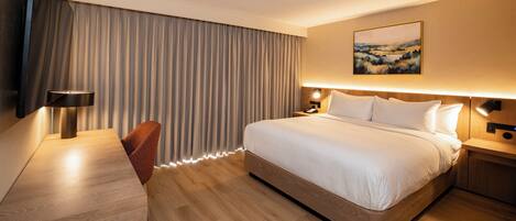 A modern hotel room with a large bed, a desk with a chair, a flat-screen TV, and a painting on the wall.