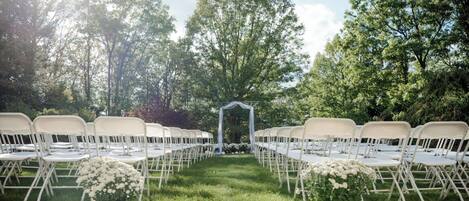 An outdoor wedding venue with rows of white folding chairs and a central archway.