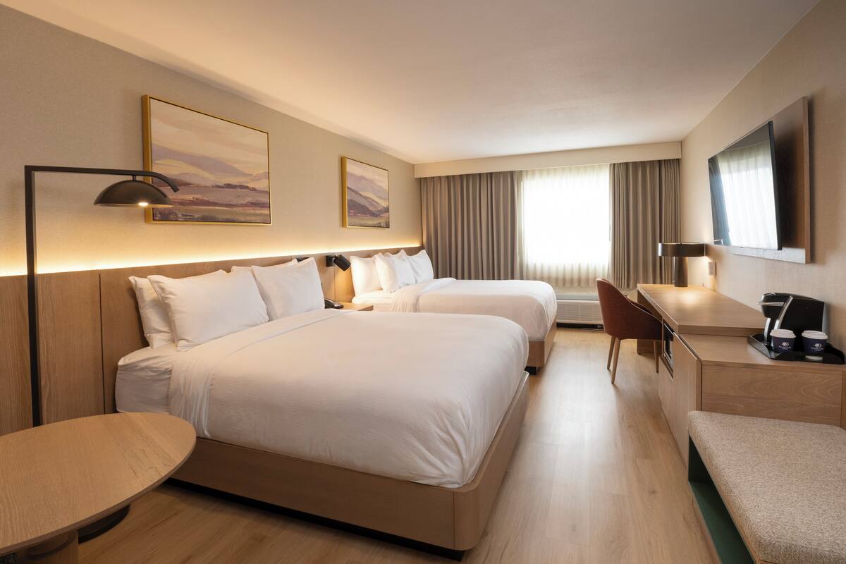A hotel room with two beds, a desk, a chair, a TV, and a painting on the wall.