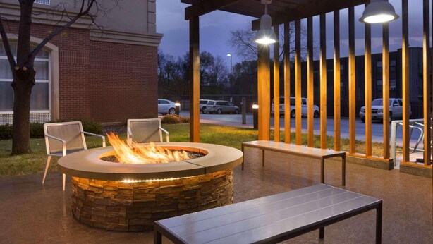 An outdoor patio area with a stone fire pit, seating, and a pergola with hanging lights.