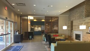 A modern lobby with a reception desk, seating area, and a kitchen in the background.